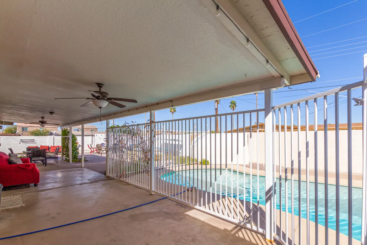 This image showcases the private swimming pool at the heart of the backyard, surrounded by palm trees, a covered patio, and comfortable outdoor furniture. The scene is relaxed and inviting, suggesting opportunities for swimming, lounging, and outdoor dining under the Arizona sun.