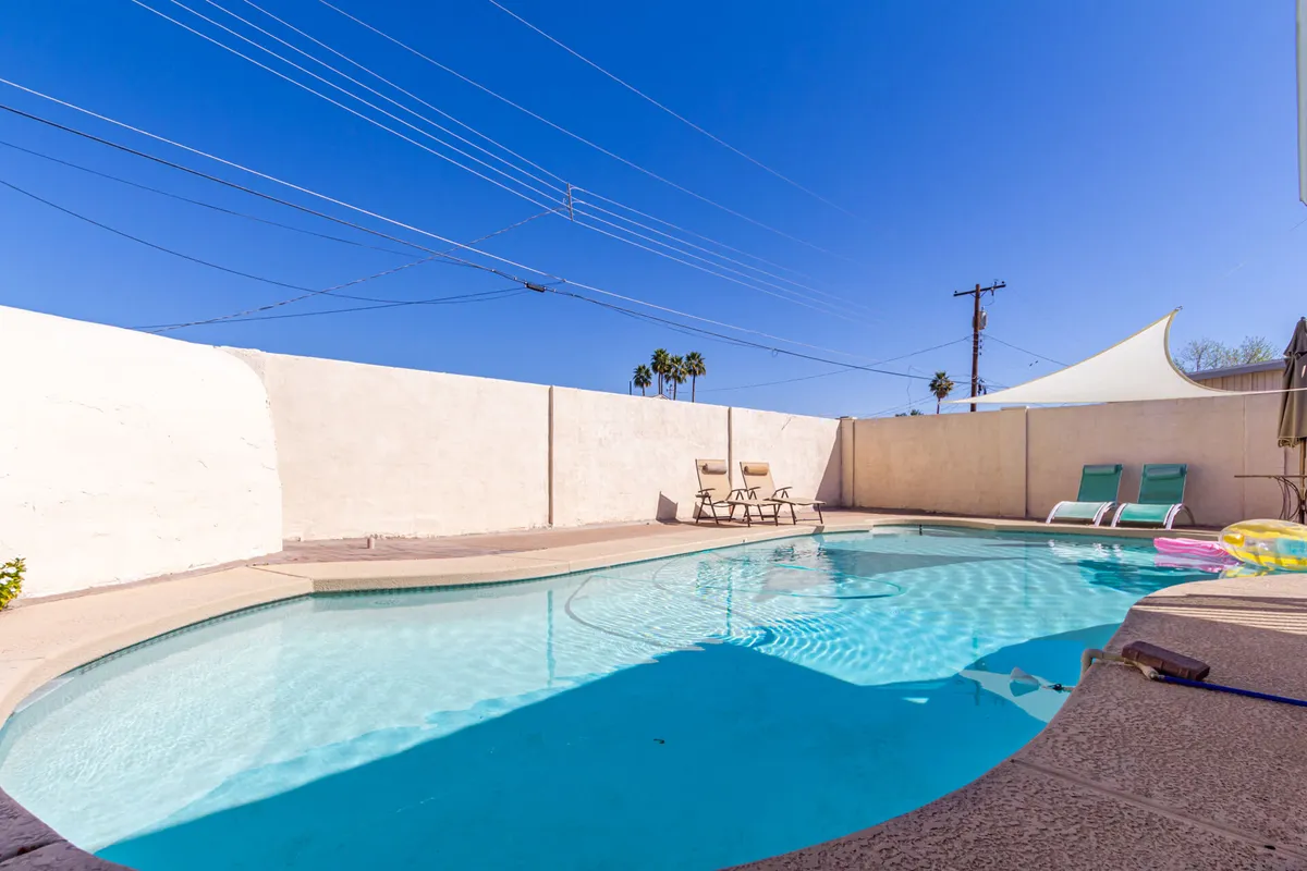 This image showcases a sparkling swimming pool surrounded by lounge chairs, a modern shade sail, and palm trees, all set within a sunny Arizona outdoor space. The pool area invites guests to relax, socialize, swim, or simply soak up the desert ambiance. The vibrant setting hints at leisurely mornings with coffee poolside and offers a tranquil retreat after local adventures.