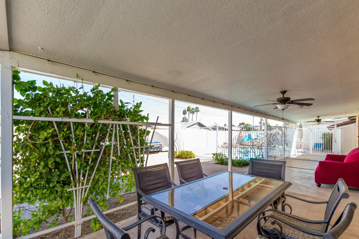 This exterior scene highlights an outdoor dining table set amid greenery, with a red chair adding a playful accent. The setting feels casual and inviting, ideal for sunset dinners, relaxing, or celebrating with loved ones.