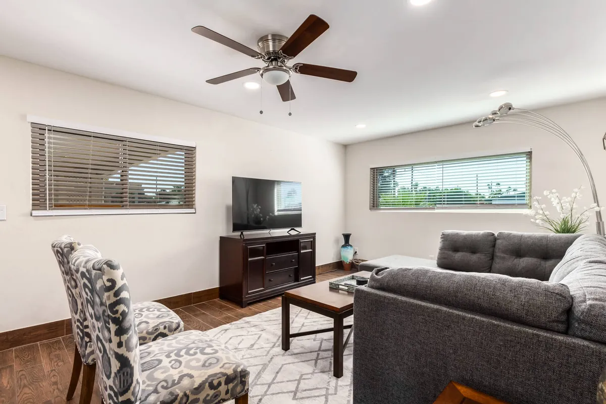 A stylish living area featuring a sofa, coffee table, modern TV, decorative chair, and ceiling fan. The room is bathed in natural light, creating a comfortable and relaxed setting ideal for both movie marathons and quiet evenings in.
