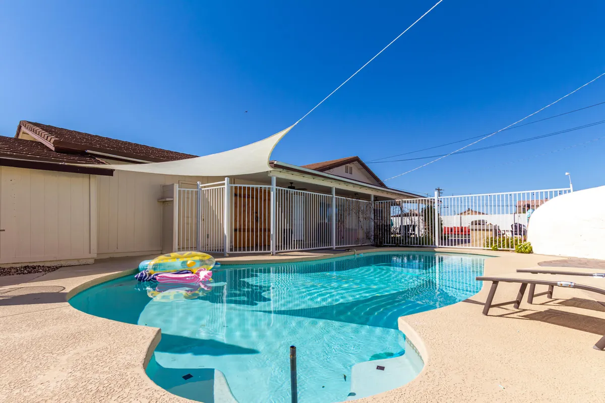 The hero image features the sparkling backyard swimming pool as the focal point, adorned with vibrant floaties and shaded by a modern sail. The pool area is enclosed by a privacy fence, creating an inviting space for sunbathing, swimming, and gathering with friends or family in a joyful, relaxed atmosphere.