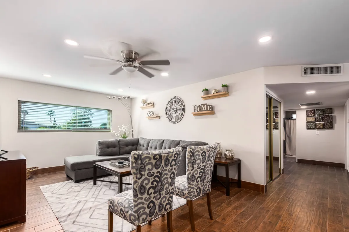 An open-plan space with a sofa, roomy dining table, decorative wall shelves, and a large clock. The flow from living to dining area is seamless, framed by tasteful decor and soft lighting that enhances the welcoming ambiance.