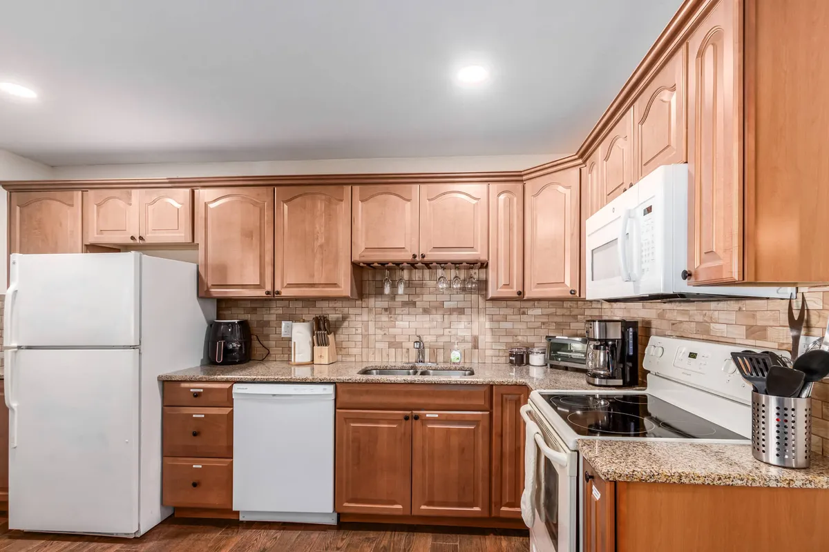 This image features a kitchen with warm wood cabinetry, sleek granite countertops, stainless steel appliances, and an inviting backsplash. The space is clearly designed for both practical meal prep and gathering, with enough room for cooking family feasts or quick breakfasts.