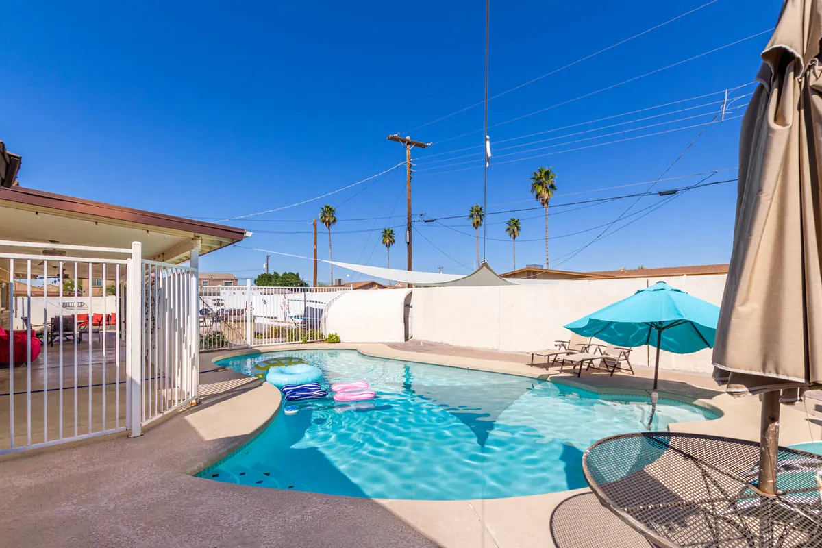This exterior image showcases a sparkling swimming pool surrounded by lounge chairs, umbrellas, and colorful pool floats, with ample space for sunbathing, barbecuing, and socializing. The lush landscaping and inviting pool area exude a leisurely, private retreat atmosphere.