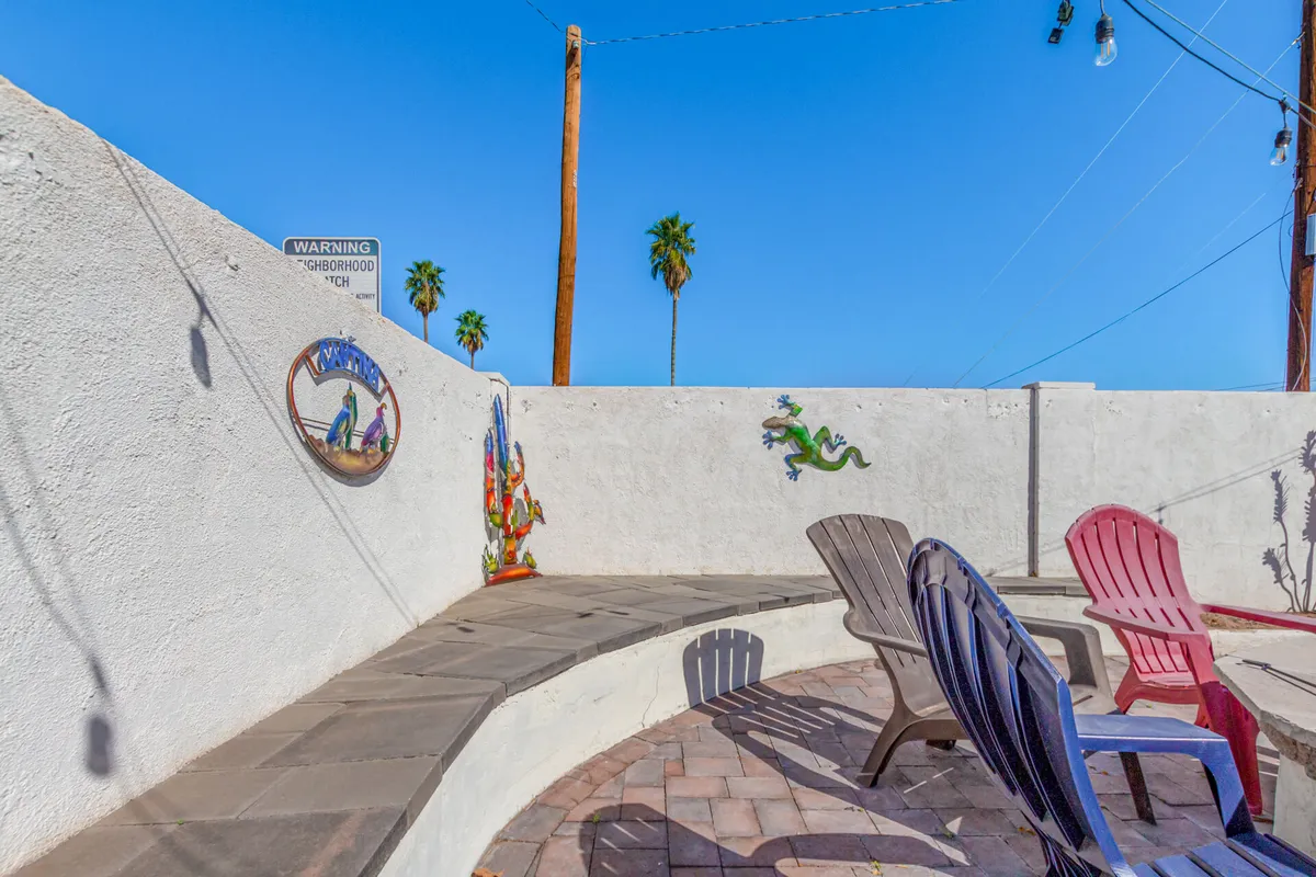 An exterior view of a cheerful, curved seating area surrounded by palm trees and vibrant wall art. The scene suggests a welcoming space for community, relaxation, and lively group conversation, set against a blue sky backdrop.