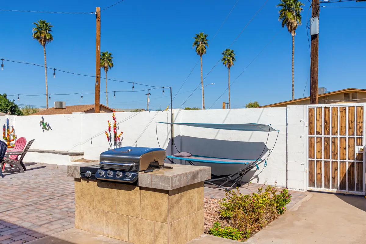 A laid-back outdoor space is shown with a BBQ grill, hammock, palm trees, and a comfortable seating area. The setting invites gatherings for barbecues and relaxation, with the ambiance perfect for sunset dinners and starlit evenings.