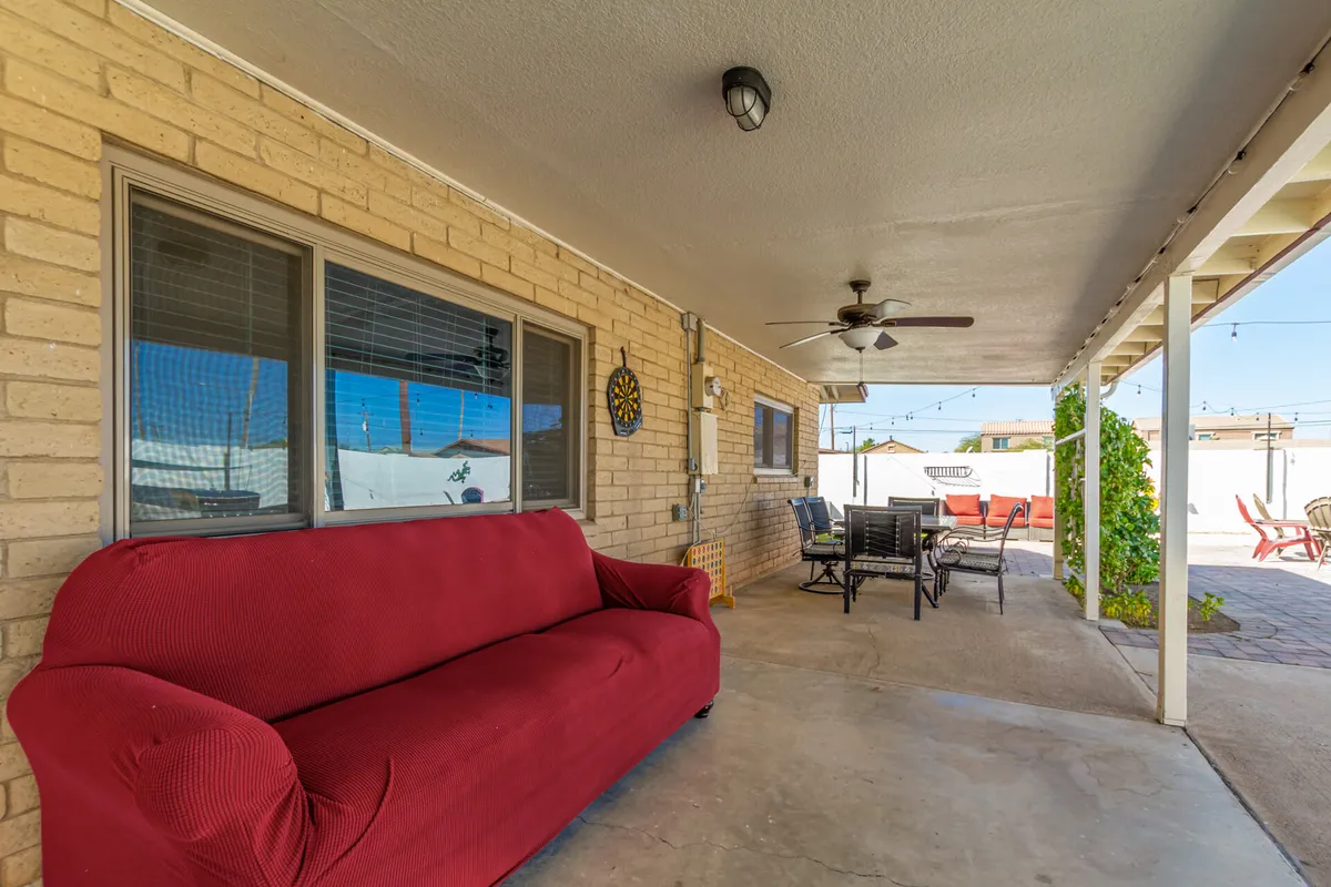 This image features a vibrant red couch next to an outdoor dining set, complemented by a decorative wall clock. The space transitions seamlessly between indoor comfort and outdoor living, suggesting the enjoyment of sunset dinners, lively game nights under string lights, and sociable afternoons in the fresh air.